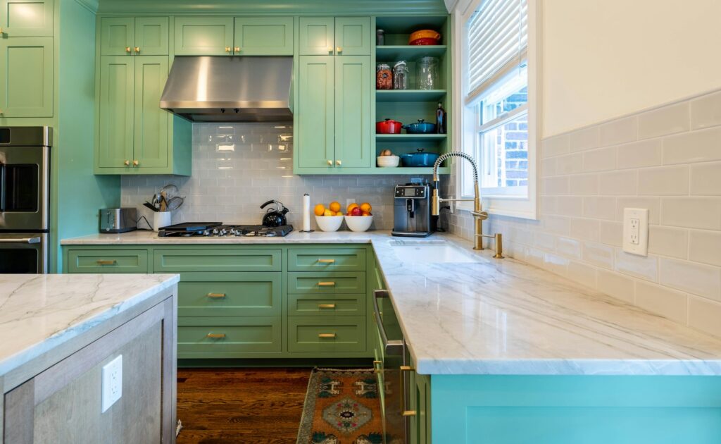 A kitchen with green cabinets and marble worktops, showing a bold colour update