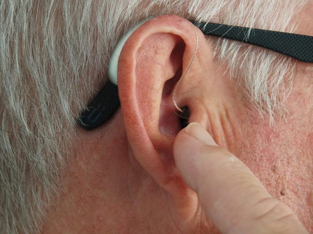 Person wearing silver-framed glasses with a small, discreet hearing aid