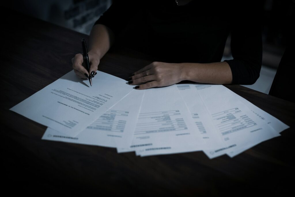 A woman signing a contract with a ballpoint pen at a table covered in papers