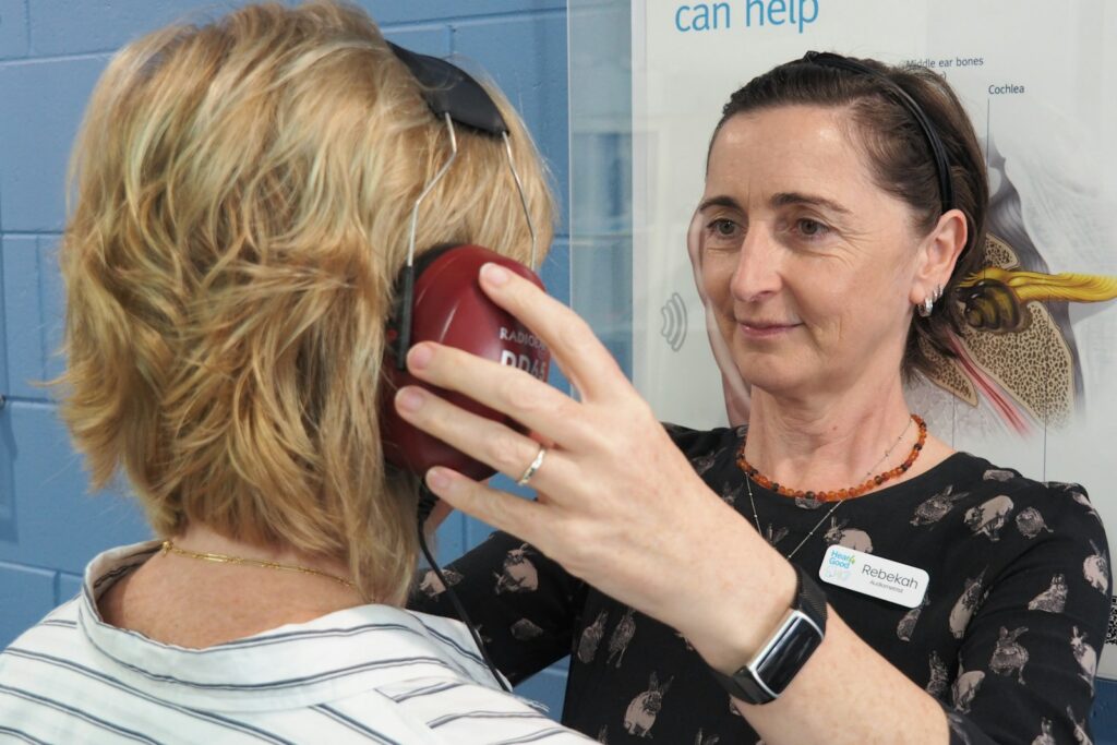 An audiologist helping a woman with a hearing test, with headphones placed on her before testing