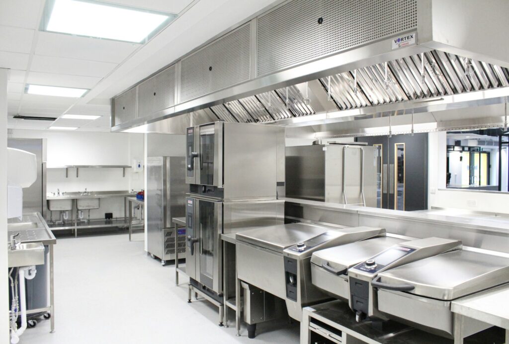 Commercial kitchen fit-out with stainless steel worktops and an extraction canopy above the cooking equipment
